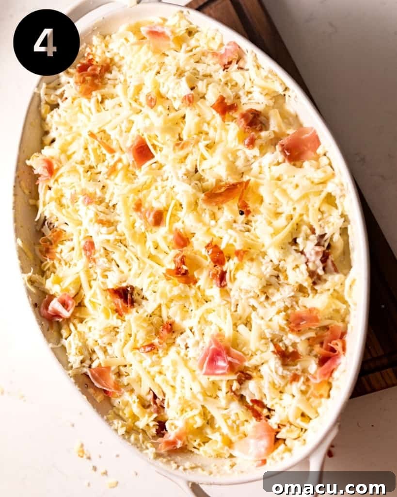 A baking dish filled with macaroni pasta, generously topped with the creamy cheese sauce and crispy prosciutto, ready for its final transformation in the oven.