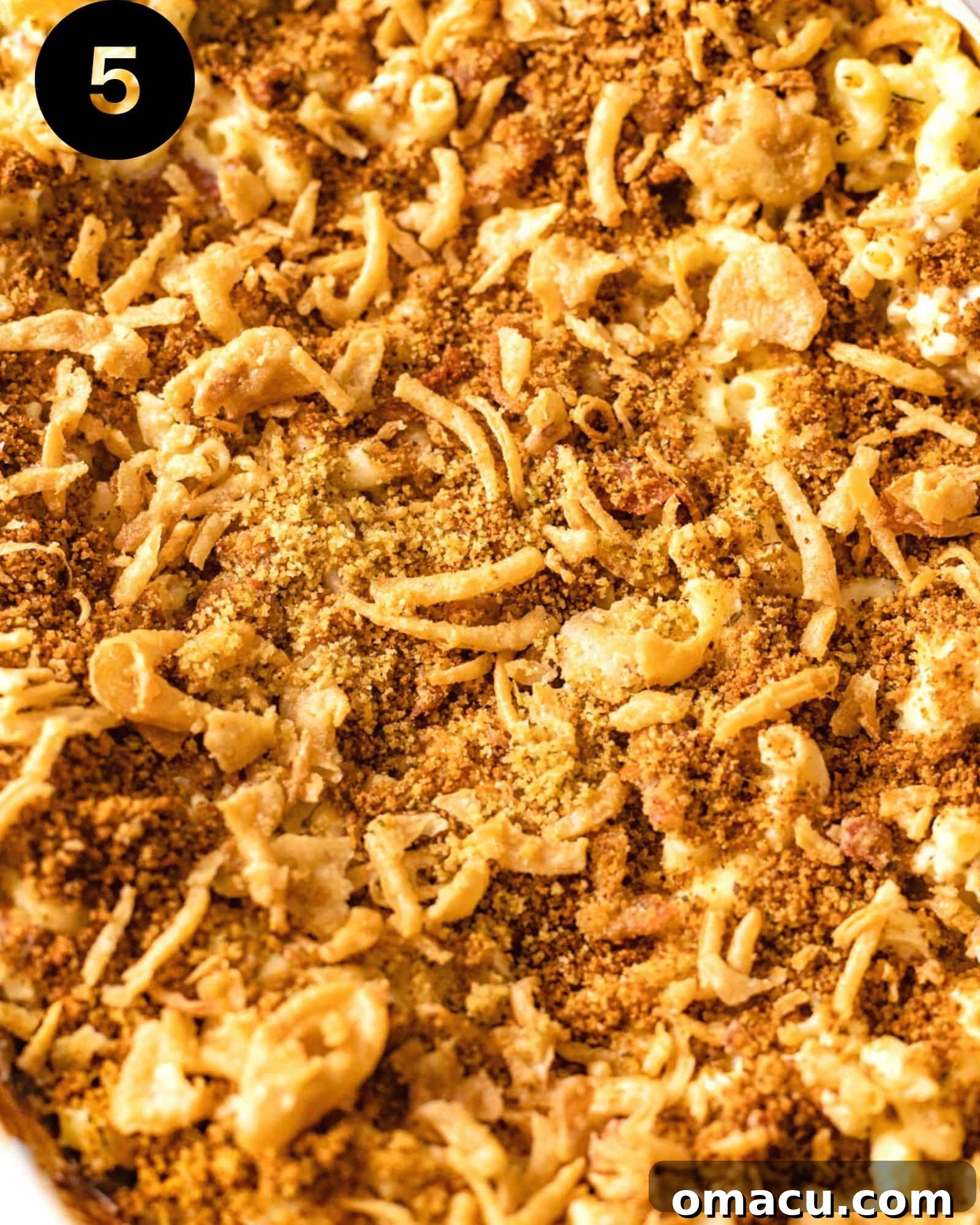A close-up view of the irresistible golden-brown breadcrumb topping, interspersed with crispy French onions, crowning the rich macaroni and cheese.