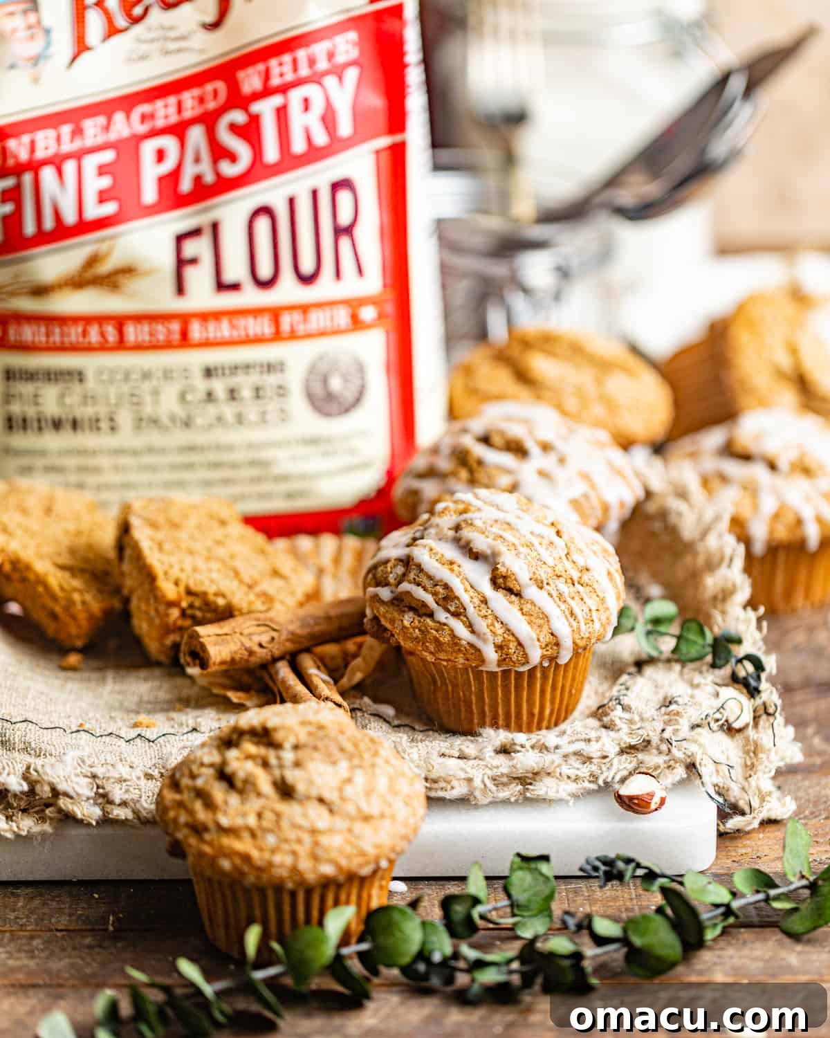 A beautifully glazed gingerbread muffin rests on a rustic wooden table, with a bag of pastry flour, a key ingredient, softly visible in the background.