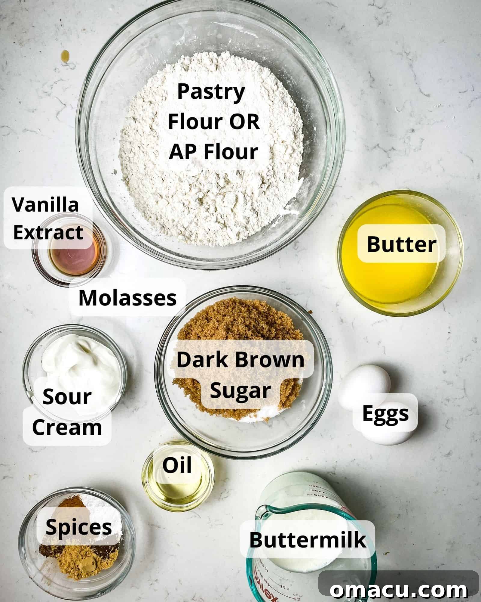A beautifully arranged selection of ingredients for gingerbread muffins, including pastry flour, rich butter, creamy buttermilk, fresh eggs, an array of warm spices, dark brown sugar, granulated sugar, smooth sour cream, neutral oil, and fragrant vanilla extract.