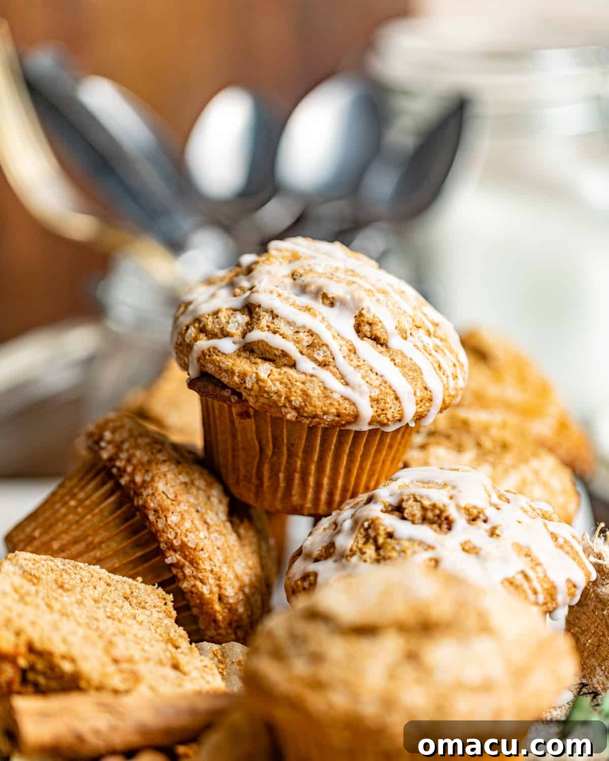 A delightful stack of gingerbread muffins, perfectly golden and inviting, arranged in front of a decorative glass jar filled with an assortment of vintage spoons, adding a touch of rustic charm.