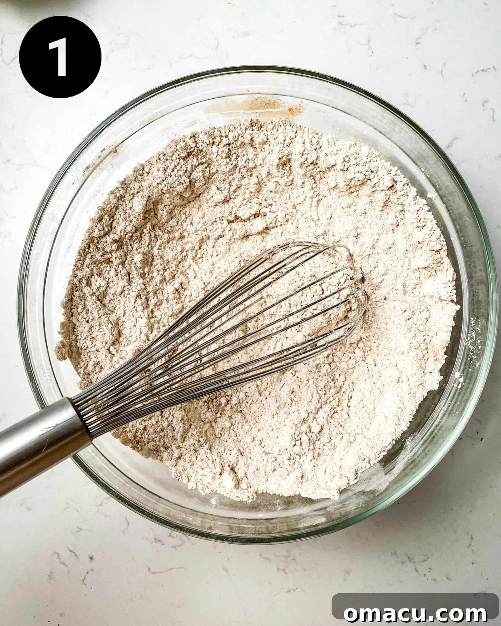 A close-up shot of a bowl containing a precisely measured mixture of flour, aromatic spices, baking soda, and baking powder, perfectly whisked together and ready for the next step.