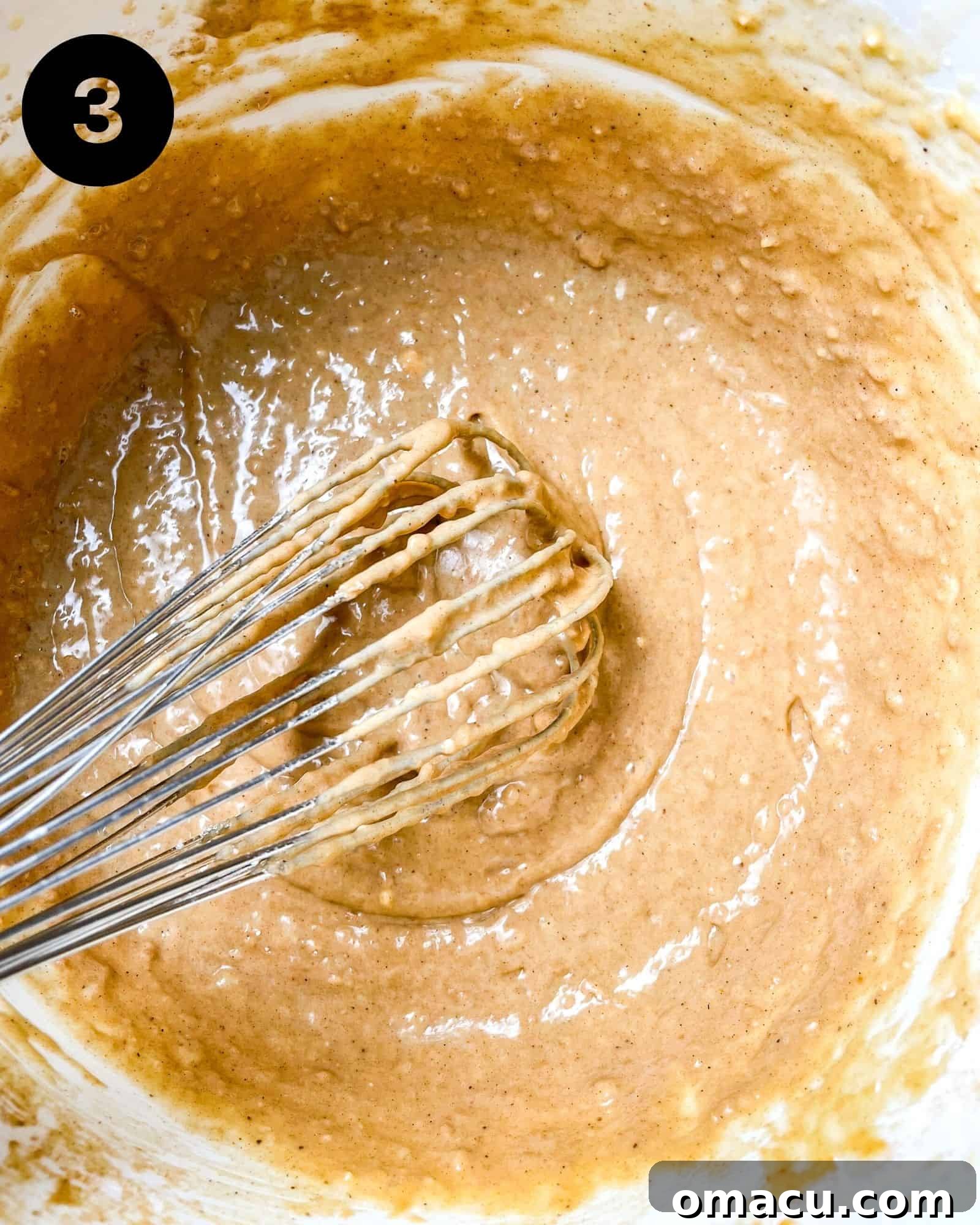 A rich, thick muffin batter in a spacious mixing bowl, with a whisk resting casually inside, indicating it's just been prepared and is ready for the next stage of baking.