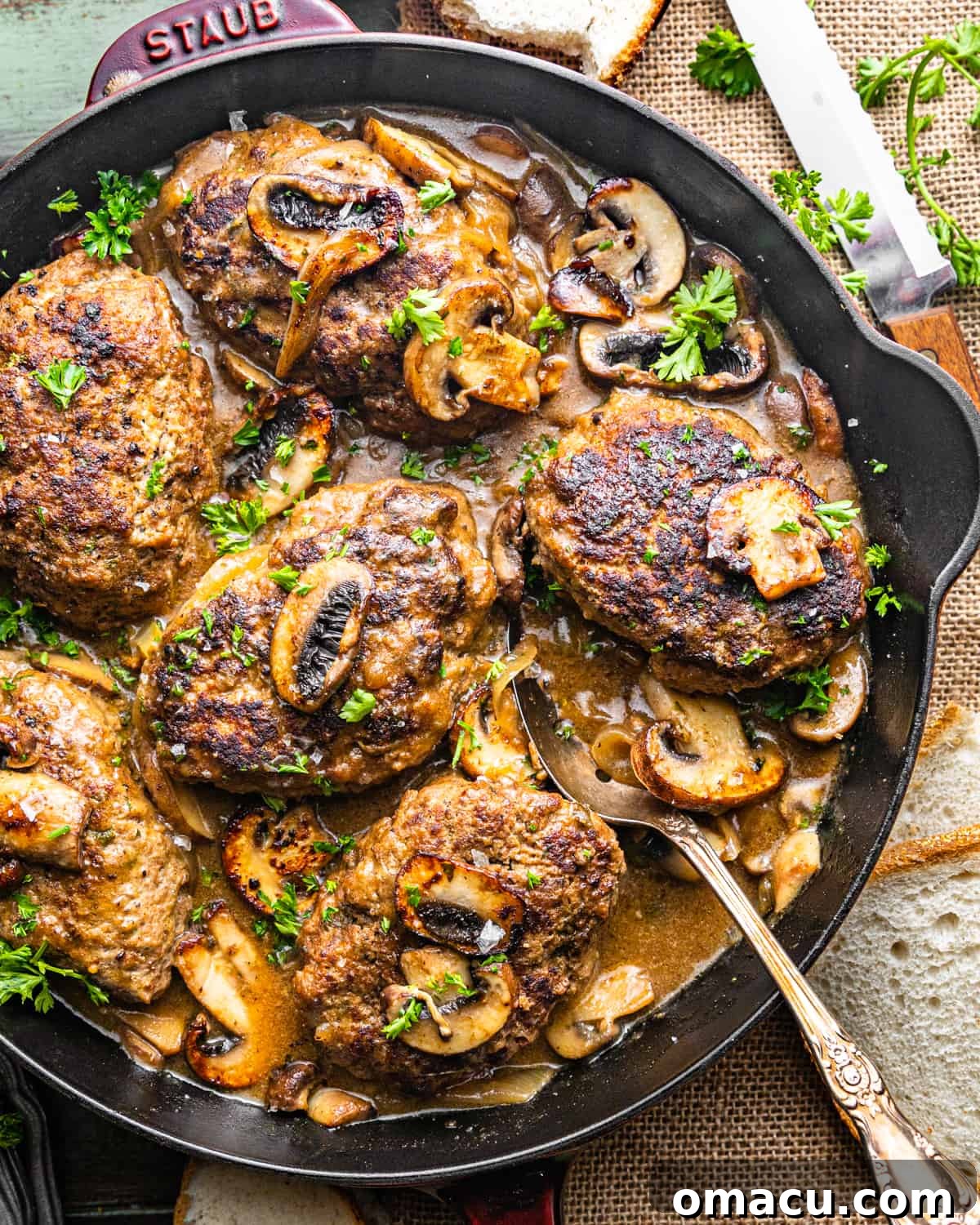 salisbury steaks in a pan with onion gravy garnished with chopped parsley.