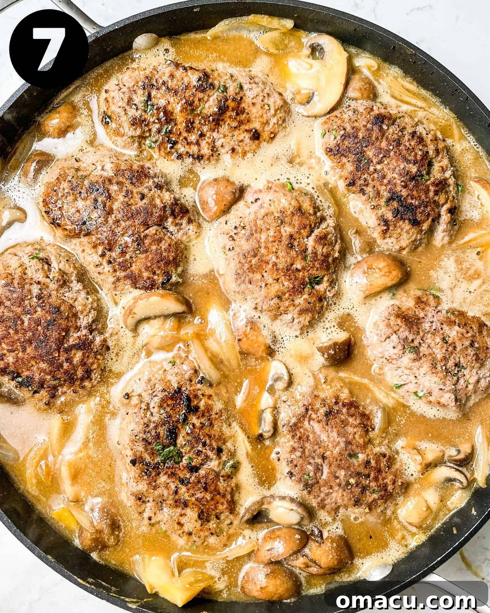 hamburger steaks in a skillet with mushrooms, onions, and gravy.
