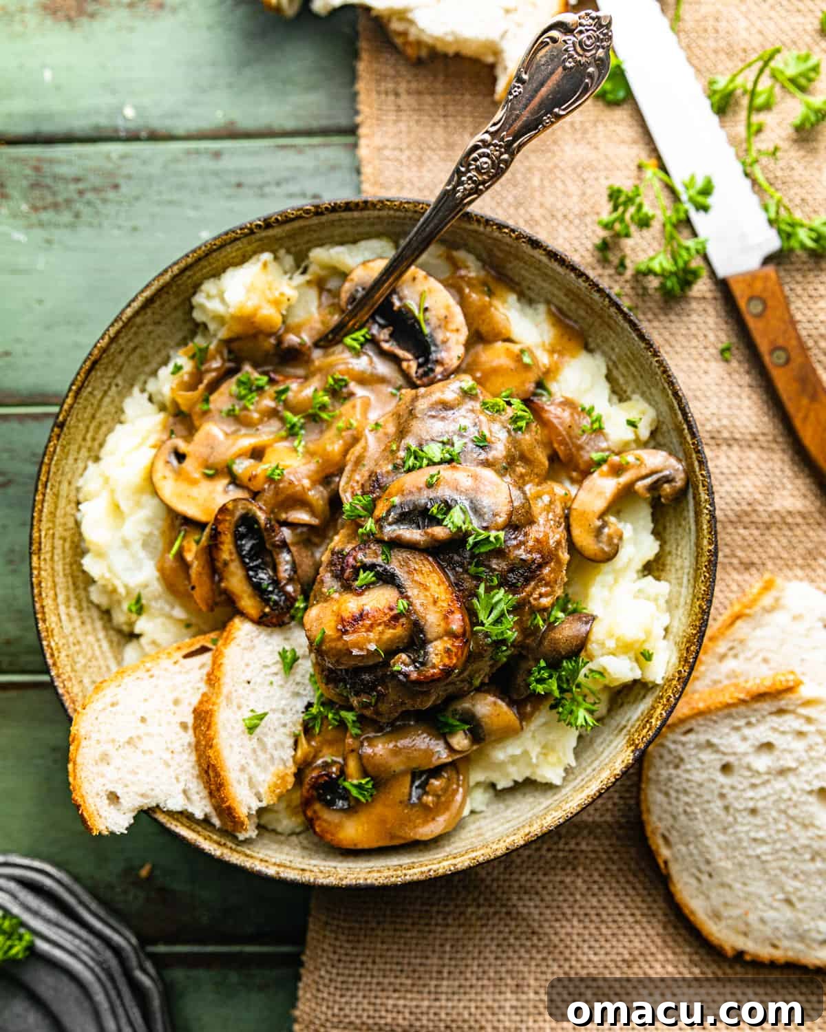 salisbury steaks in a bowl with mashed potatoes, sliced bread, and a spoon.