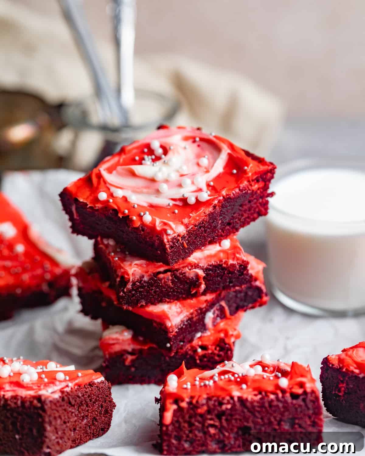 Red velvet brownies stacked high with creamy white frosting, beside a tall glass of milk, inviting a delightful dessert experience.