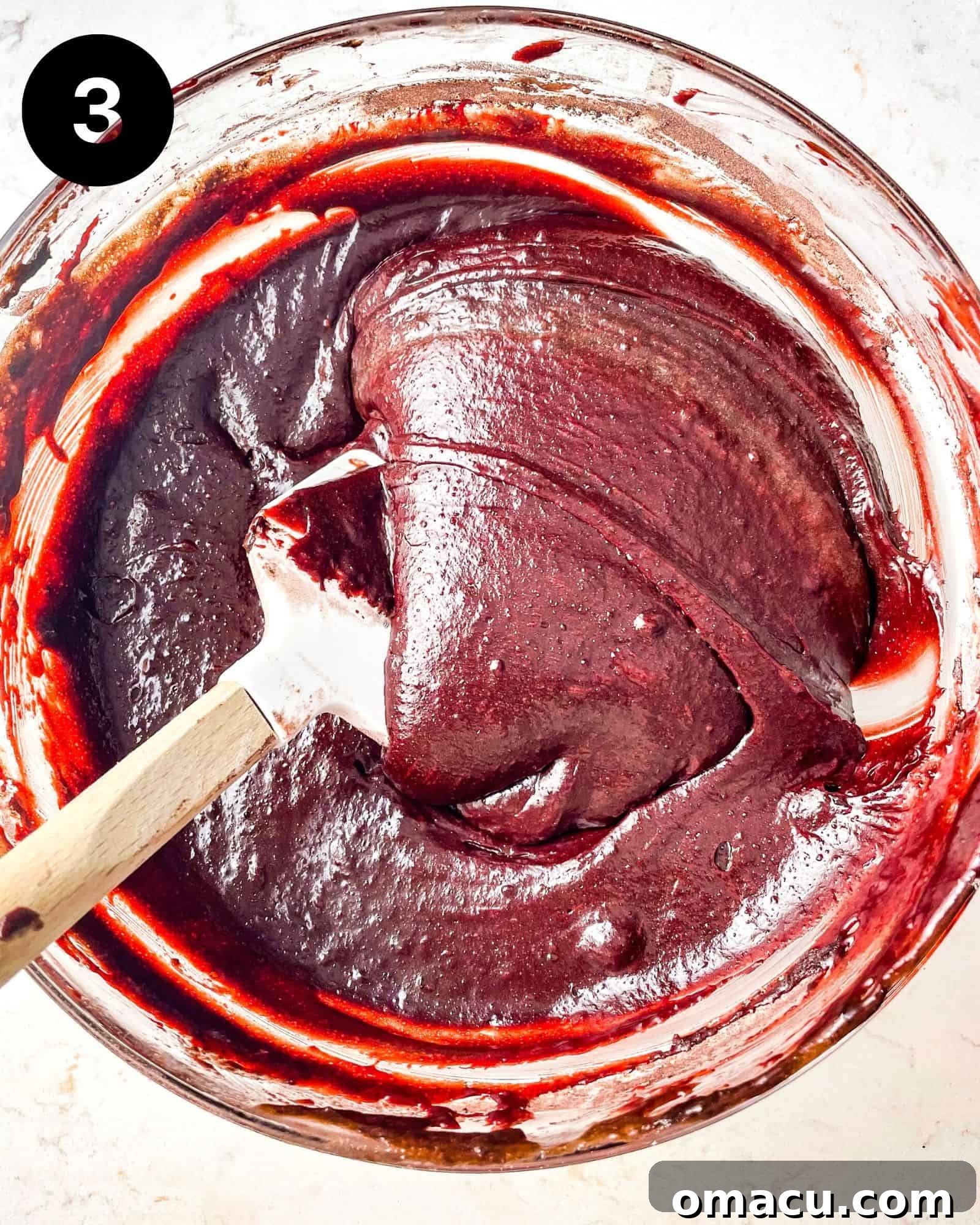 A mixing bowl containing perfectly blended red velvet brownie batter, showcasing its rich, deep red hue and smooth, inviting texture.