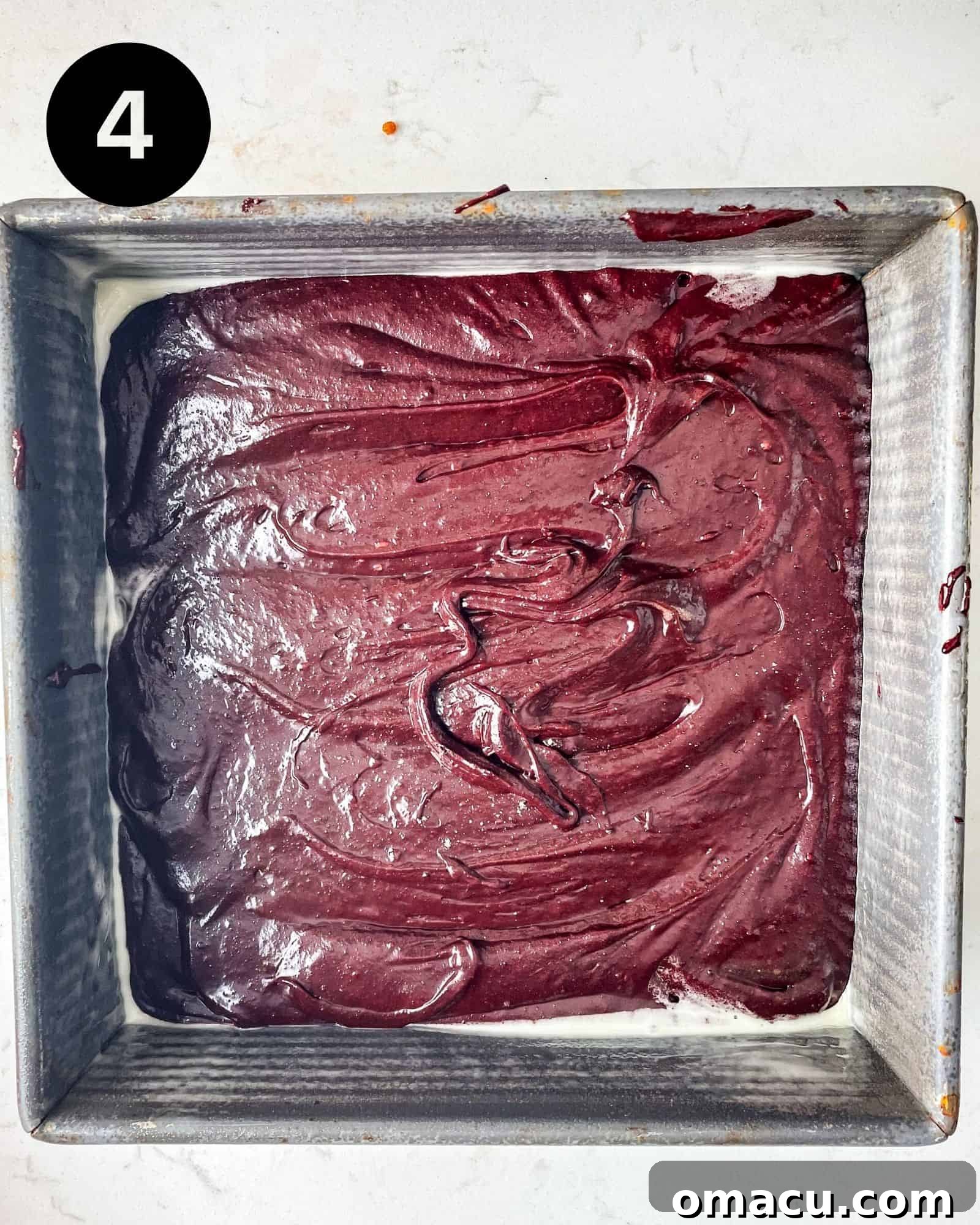 Smooth, vibrant red velvet brownie batter spread evenly in a square baking pan, ready to be baked into a delicious dessert.