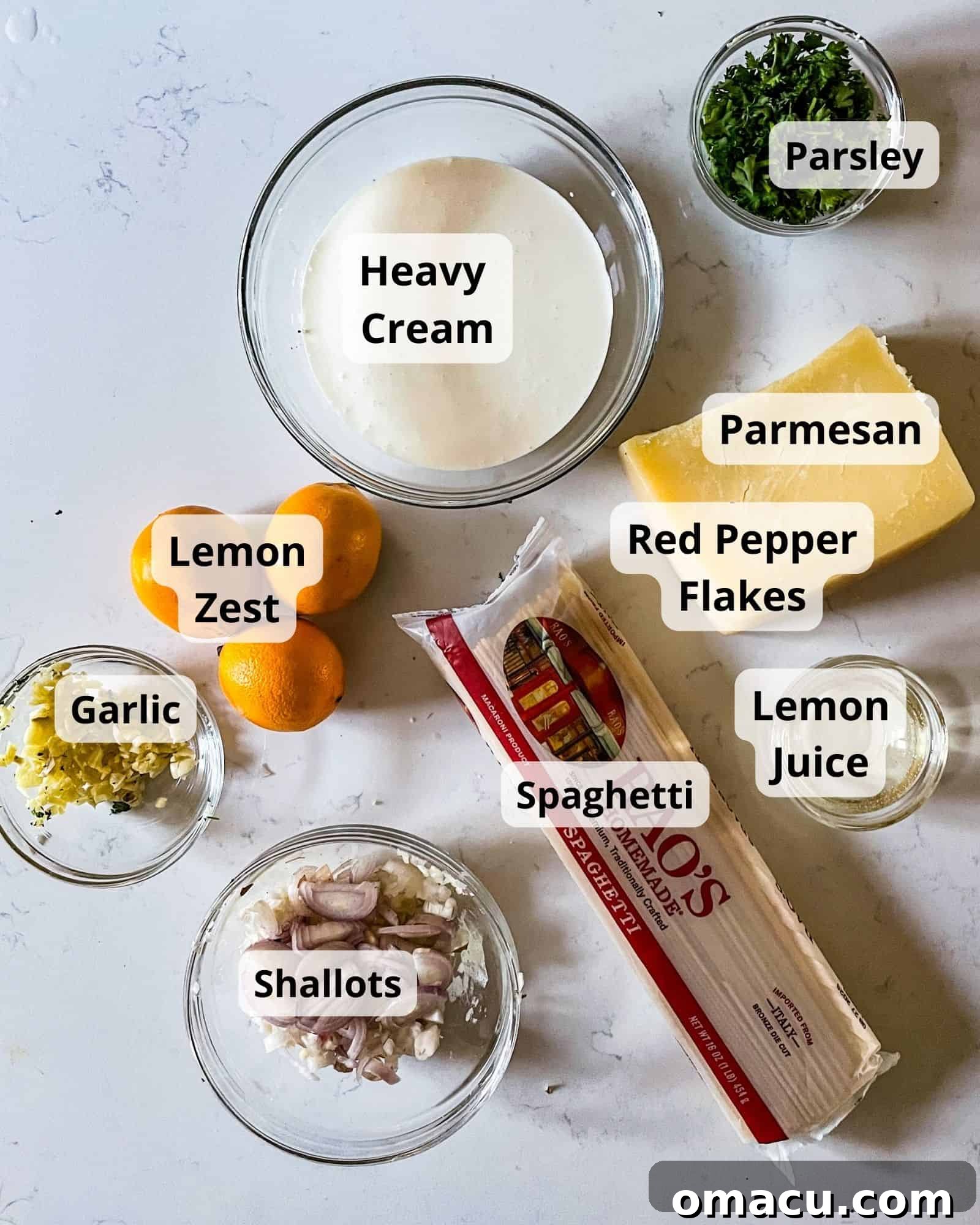 A collection of fresh ingredients laid out for making lemon garlic pasta: spaghetti, whole garlic cloves, shallots, lemon zest, heavy cream, red pepper flakes, grated Parmesan cheese, fresh lemon juice, olive oil, butter, and a bunch of fresh parsley.