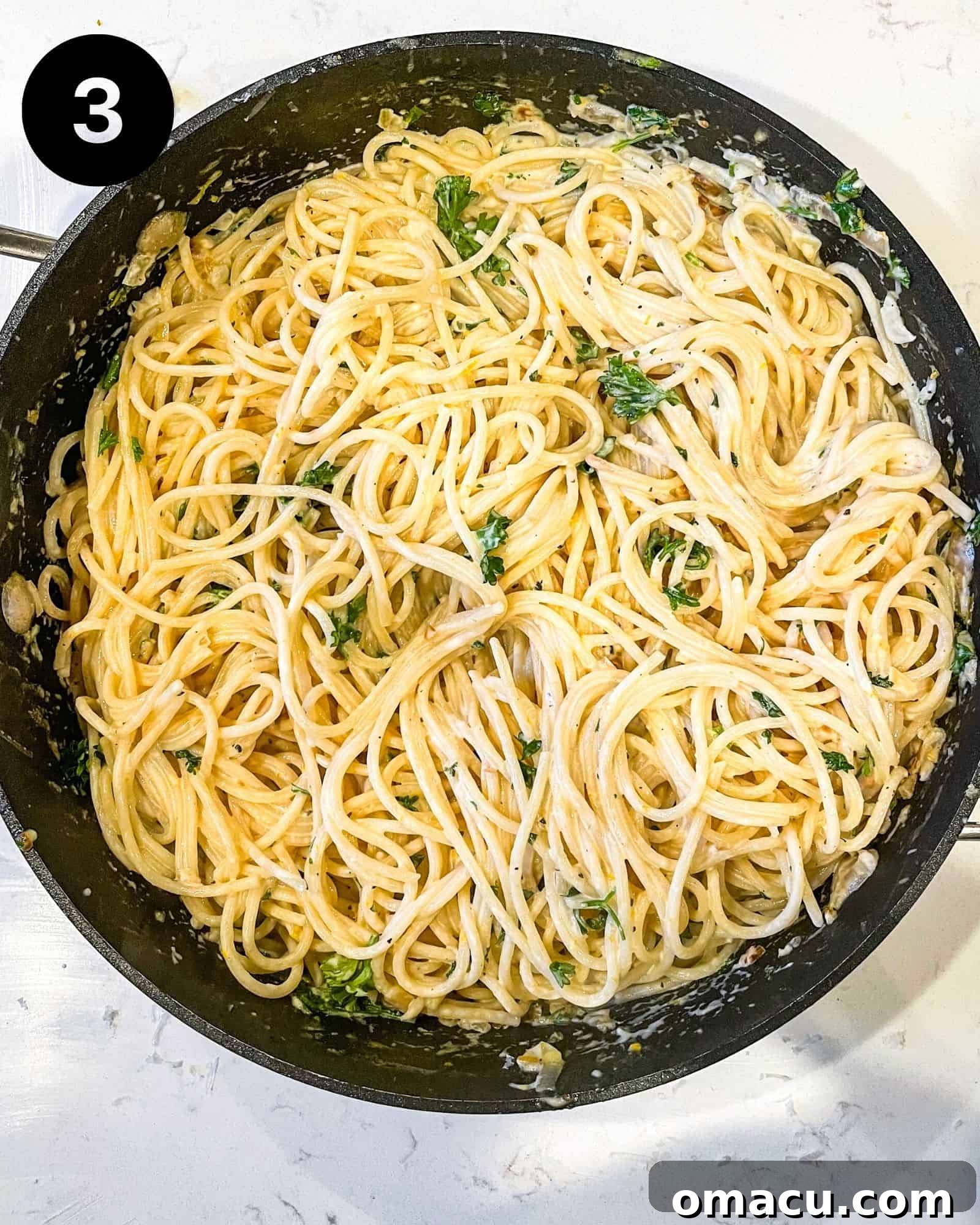 Cooked spaghetti noodles being added into a large skillet filled with the rich, creamy lemon garlic sauce, ready to be tossed together.