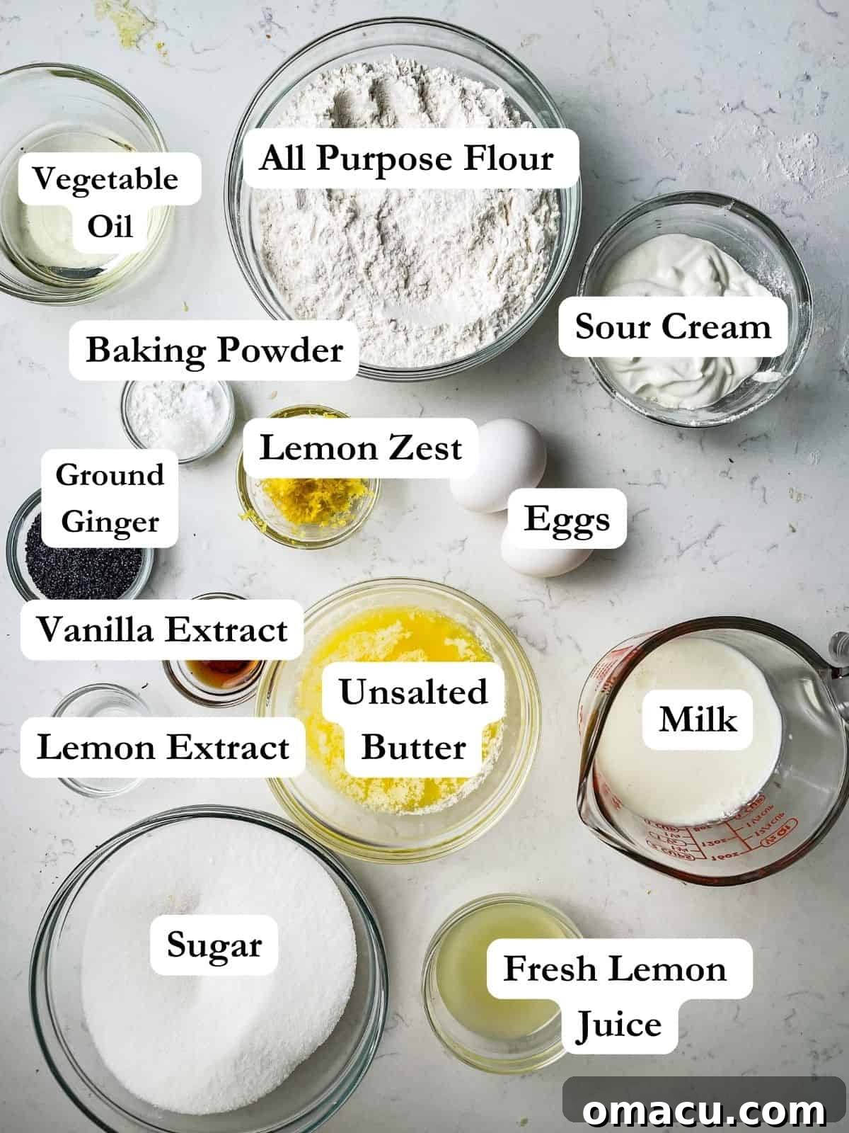 ingredients to make a lemon loaf - flour, kosher salt, baking powder, lemon zest, lemon extract, sour cream, eggs, unsalted butter, butter flavored shortening, ginger, and sugar laid out on a table.