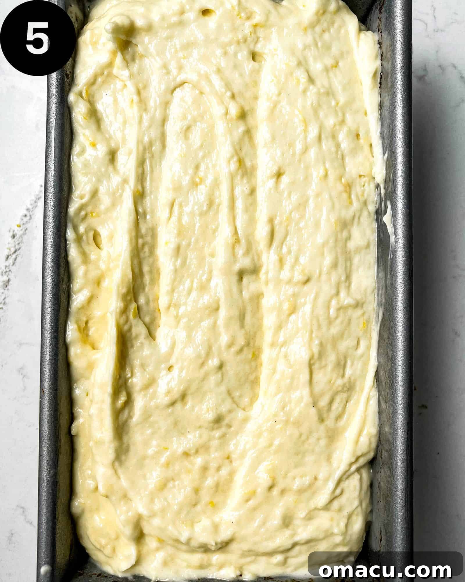 Lemon Loaf cake batter poured into a parchment-lined loaf pan, ready for the oven.