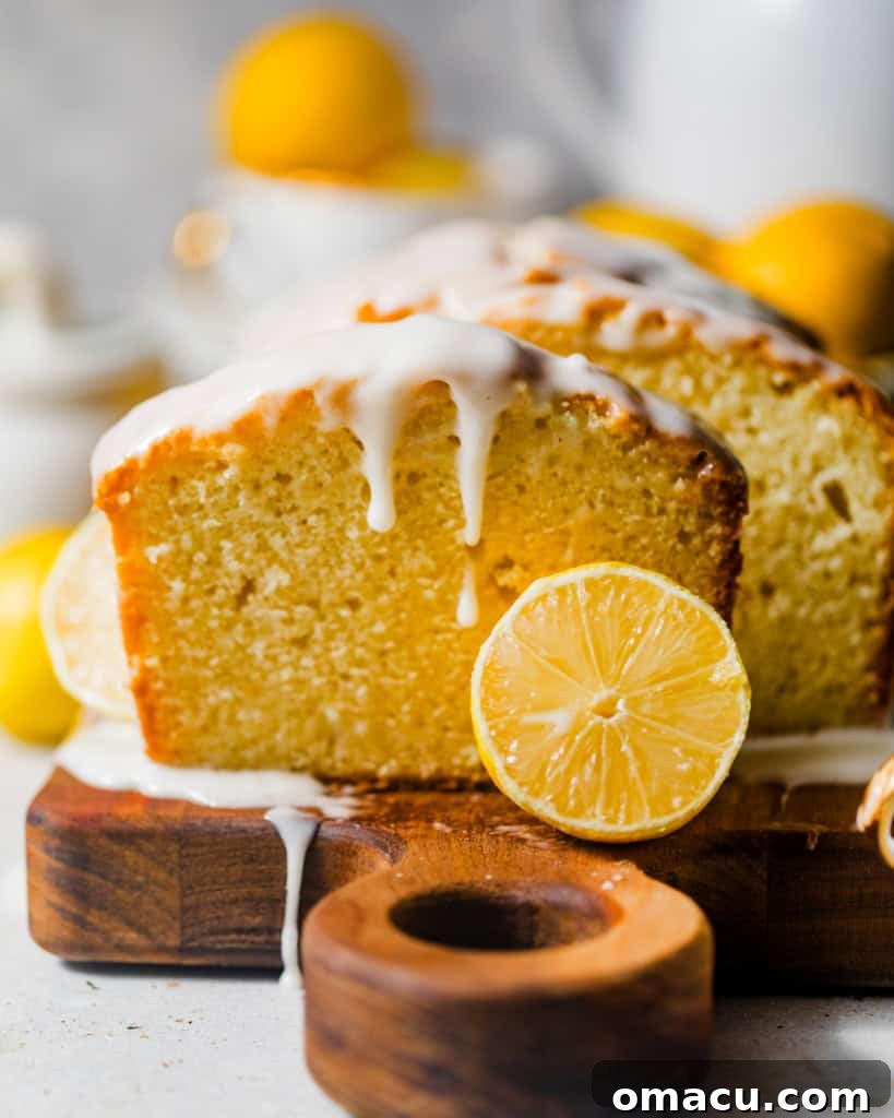 lemon loaf on a serving board topped with a generous amount of lemon glaze and garnished with sliced lemons and fresh mint.