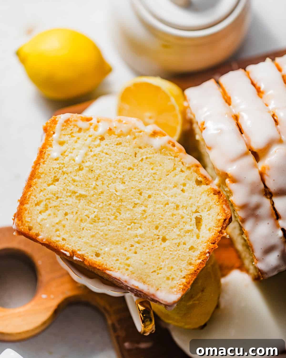 a slice of a lemon cake on top of a tea cup, garnished with lemon and a sprig of mint.