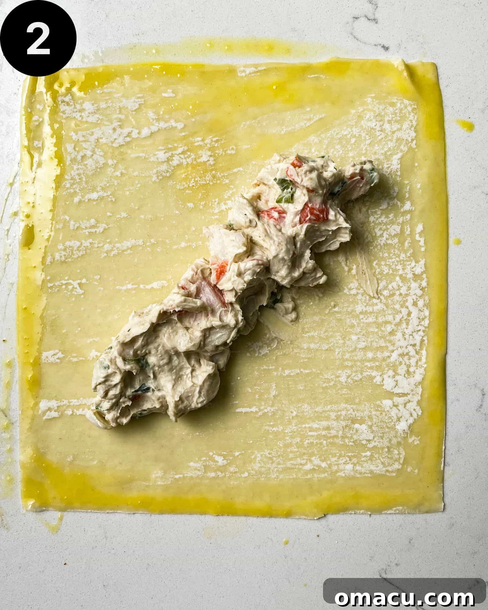 An egg roll wrapper is laid flat on a surface, with a generous portion of the creamy crab filling strategically placed in the center, ready for folding.