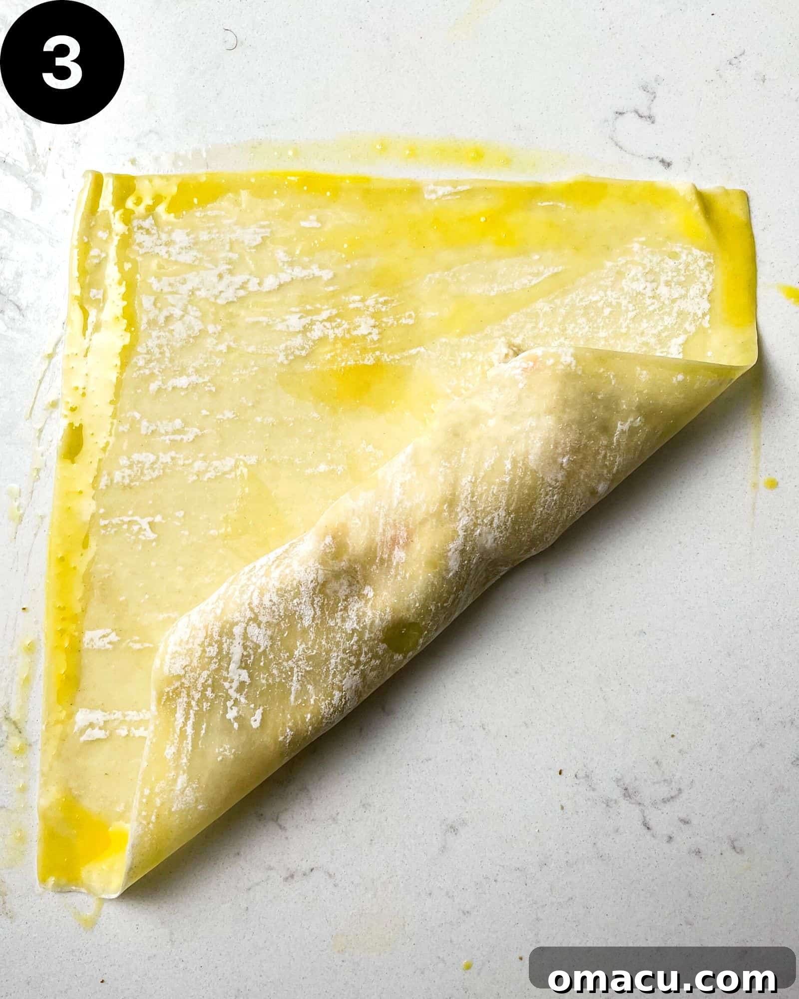 A close-up view of an egg roll wrapper, with the bottom corner folded over the filling, illustrating the first step in the wrapping process.