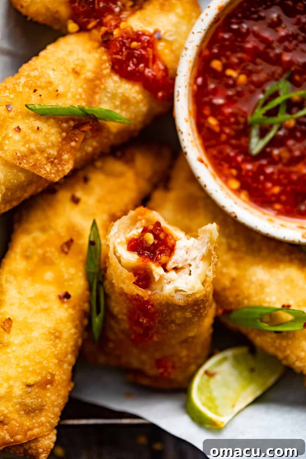 A freshly fried crab rangoon egg roll, artfully sliced in half to reveal its creamy, crab-filled interior, drizzled with sweet and sour sauce.
