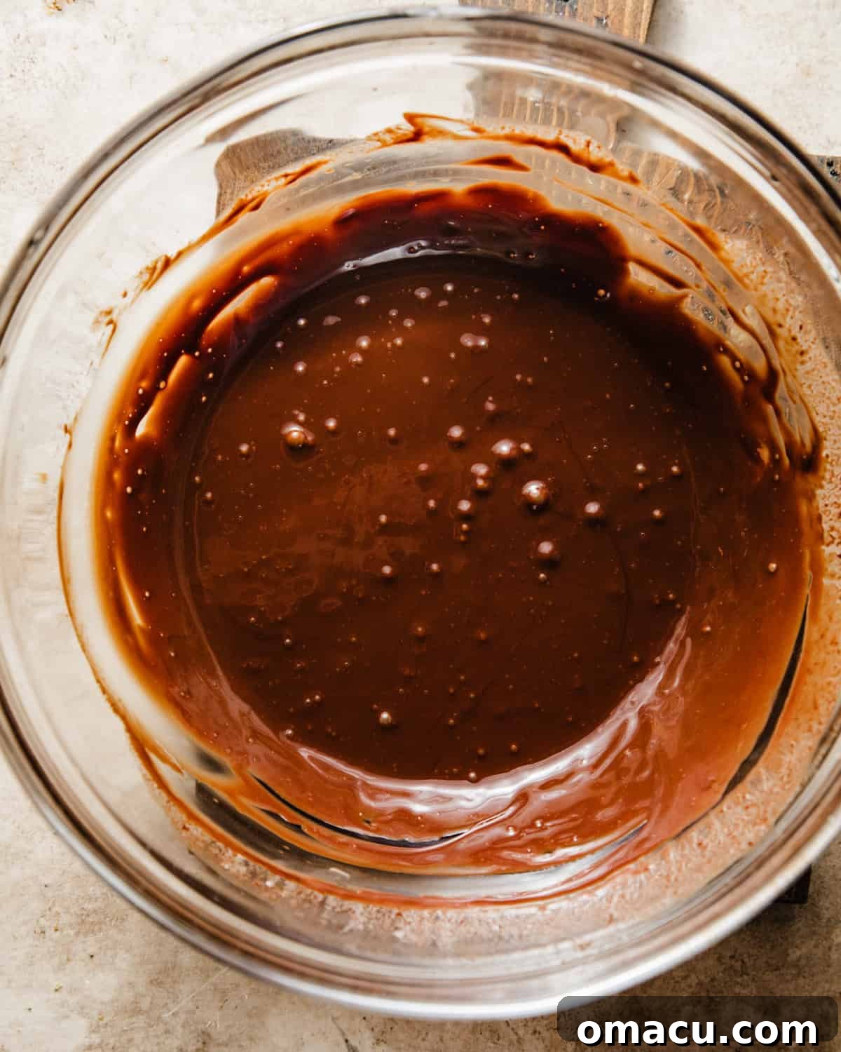A perfectly smooth and glossy chocolate ganache rests in a mixing bowl, ready to be used as a decadent topping for the muffins.