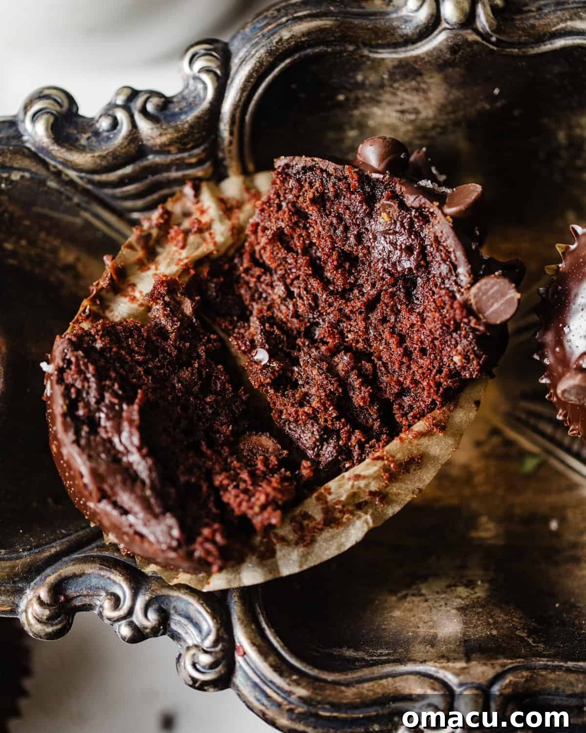 A perfectly baked triple chocolate muffin, cut in half to reveal its moist, chocolate-chip-studded interior, resting on a silver plate.