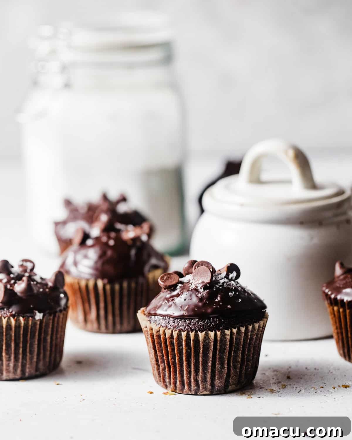 A collection of key ingredients for baking triple chocolate muffins, including flour, cocoa powder, sugar, and chocolate chips, beautifully arranged on a white surface.