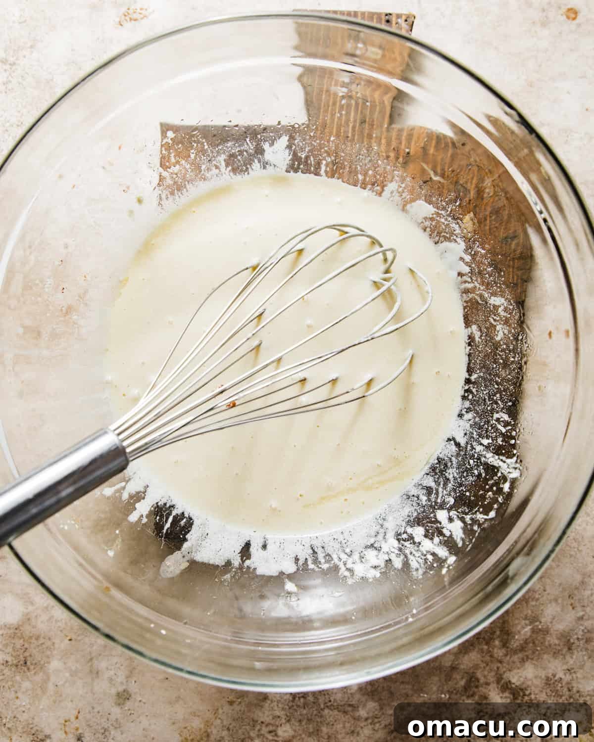 Wet ingredients, including oil, melted butter, and eggs, are being whisked together in a separate mixing bowl, creating a light and airy mixture.