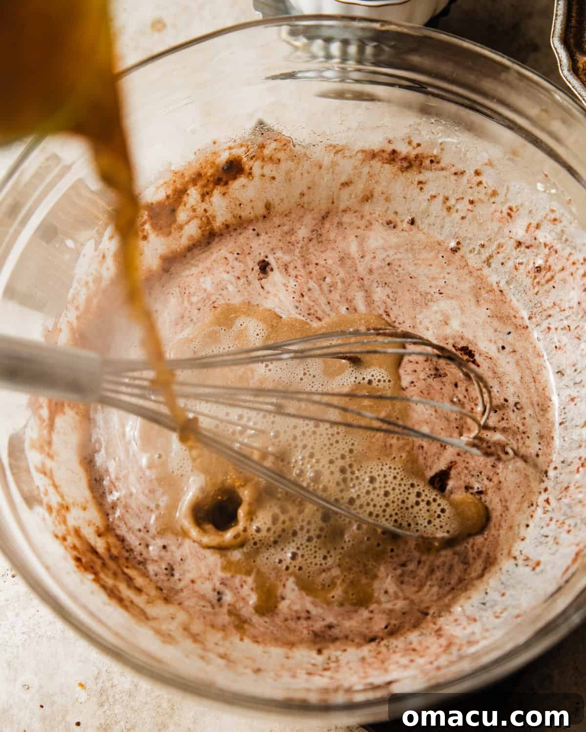 Hot coffee is being carefully poured into the chocolate muffin batter, an essential step to deepen the chocolate flavor.