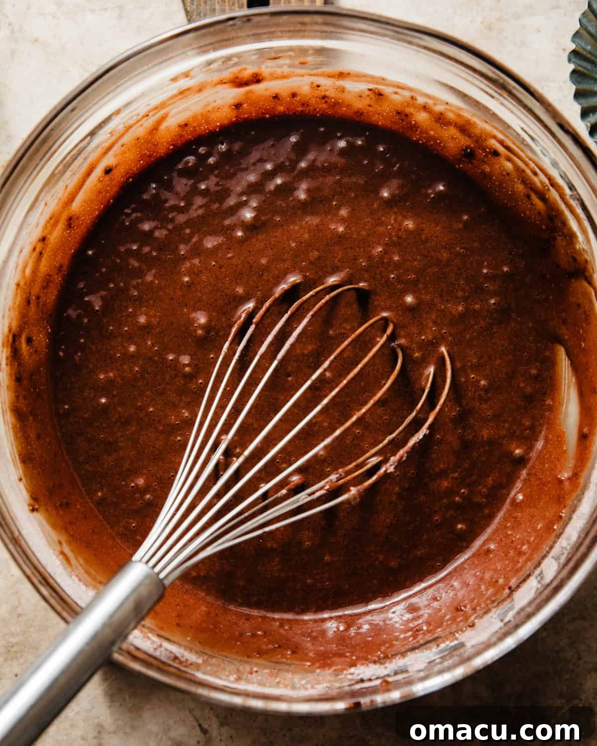 The fully mixed chocolate muffin batter, with chocolate chips folded in, is covered with plastic wrap, resting at room temperature.