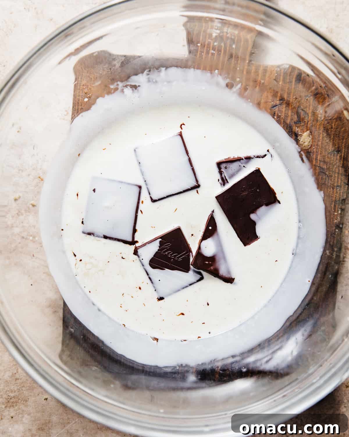 Heavy cream and dark chocolate pieces are combined in a large bowl, ready to be warmed to create a silky chocolate ganache topping.
