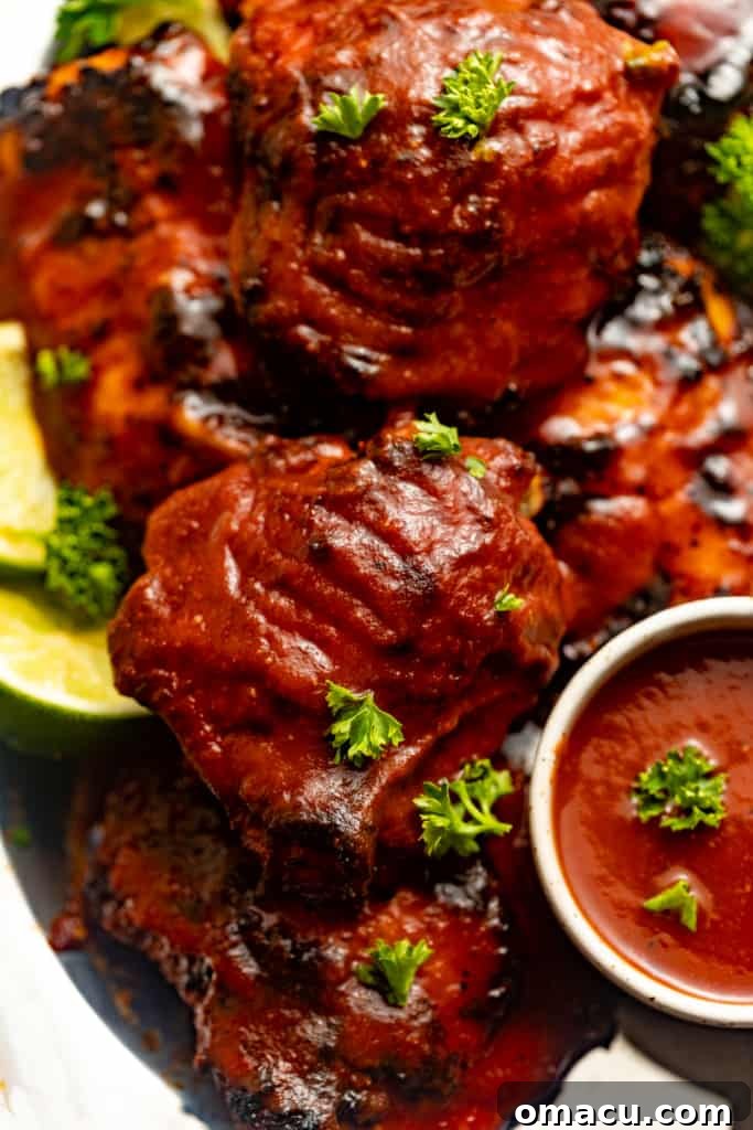 Close-up of baked chicken thighs covered in glistening BBQ sauce, served on a silver platter, ready to be enjoyed.