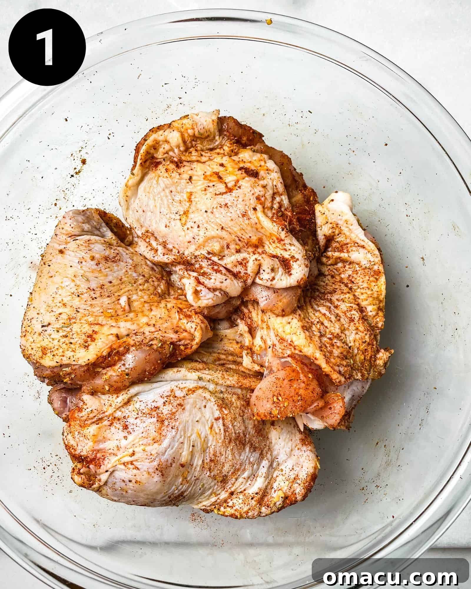 Raw chicken thighs in a mixing bowl, coated evenly with a generous layer of dry seasonings, including poultry seasoning and smoked paprika.