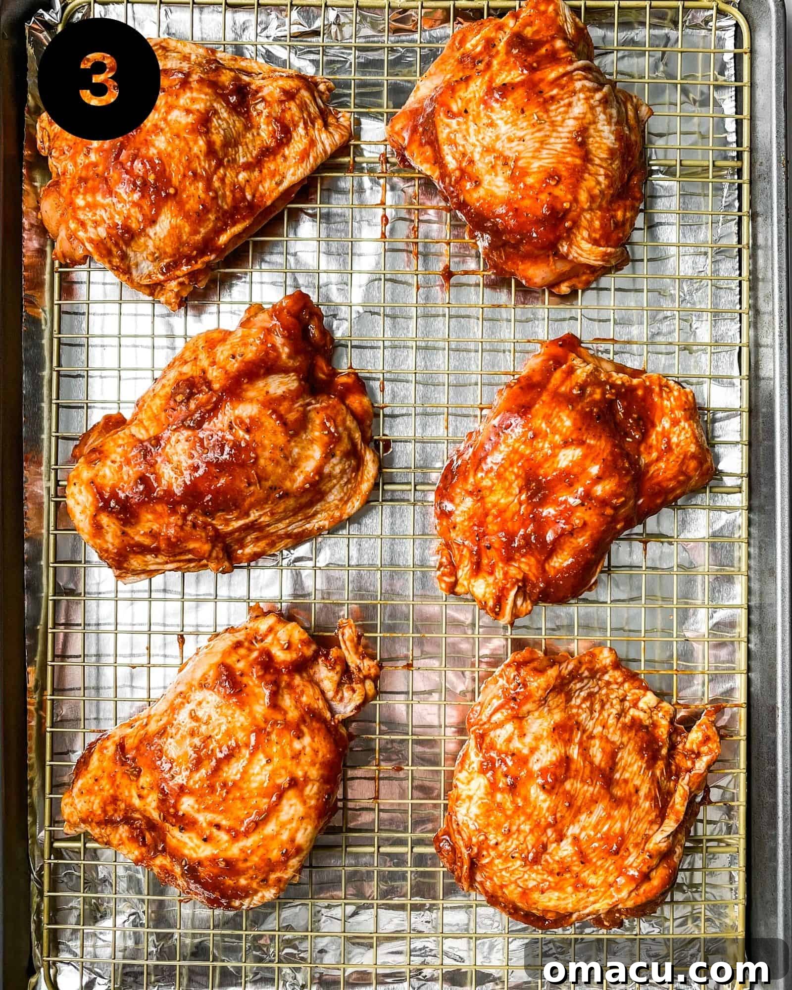 Seared chicken thighs arranged on a sheet pan, generously brushed with barbecue sauce, ready for the oven.