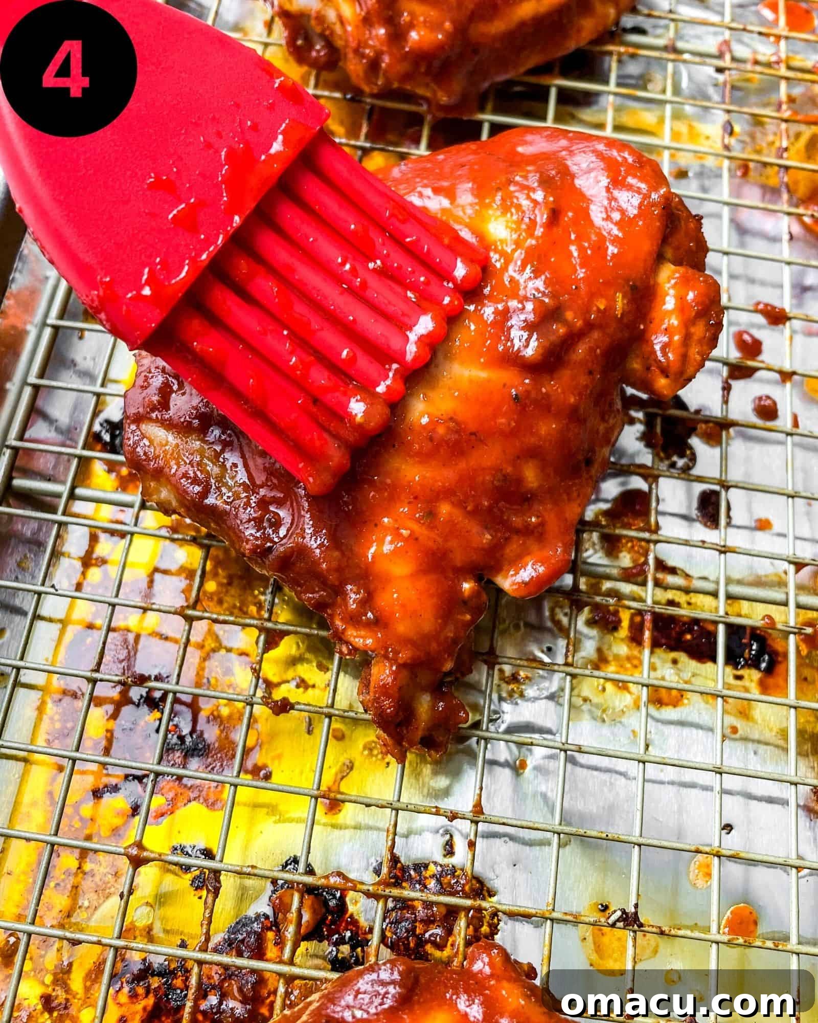 Fully baked BBQ chicken thighs resting on a wire rack over a sheet pan, coated in a rich, shiny BBQ glaze, with crispy edges.