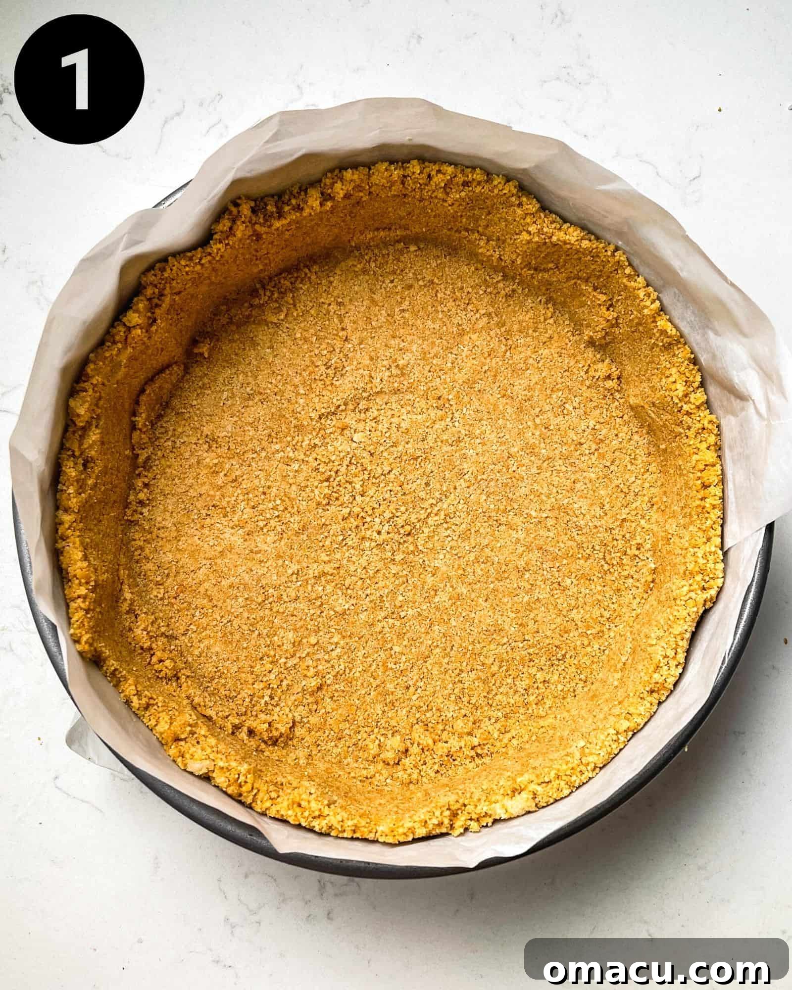 A freshly baked graham cracker crust perfectly pressed into a 9-inch springform pan, lined with parchment paper, ready for the cheesecake filling.