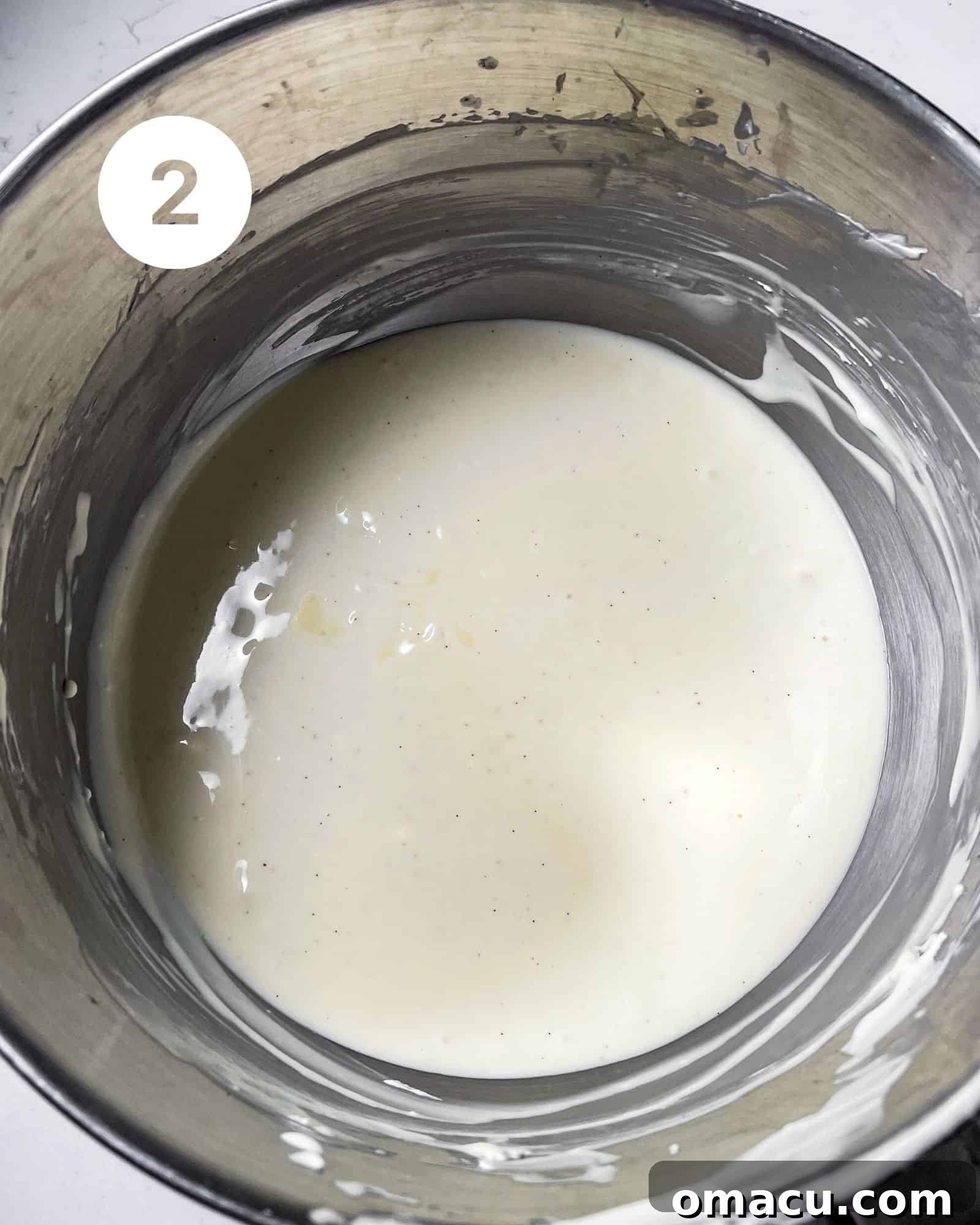 Creamy cheesecake batter being mixed in a large mixing bowl, showing its smooth consistency.