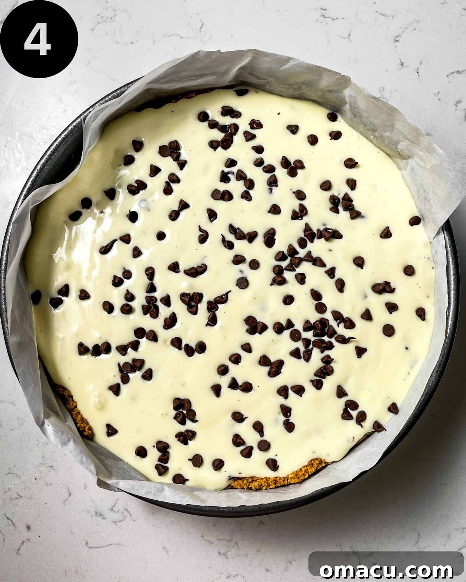 An unbaked chocolate chip cheesecake, with its creamy filling and scattered chocolate chips, resting in a parchment-lined springform pan.