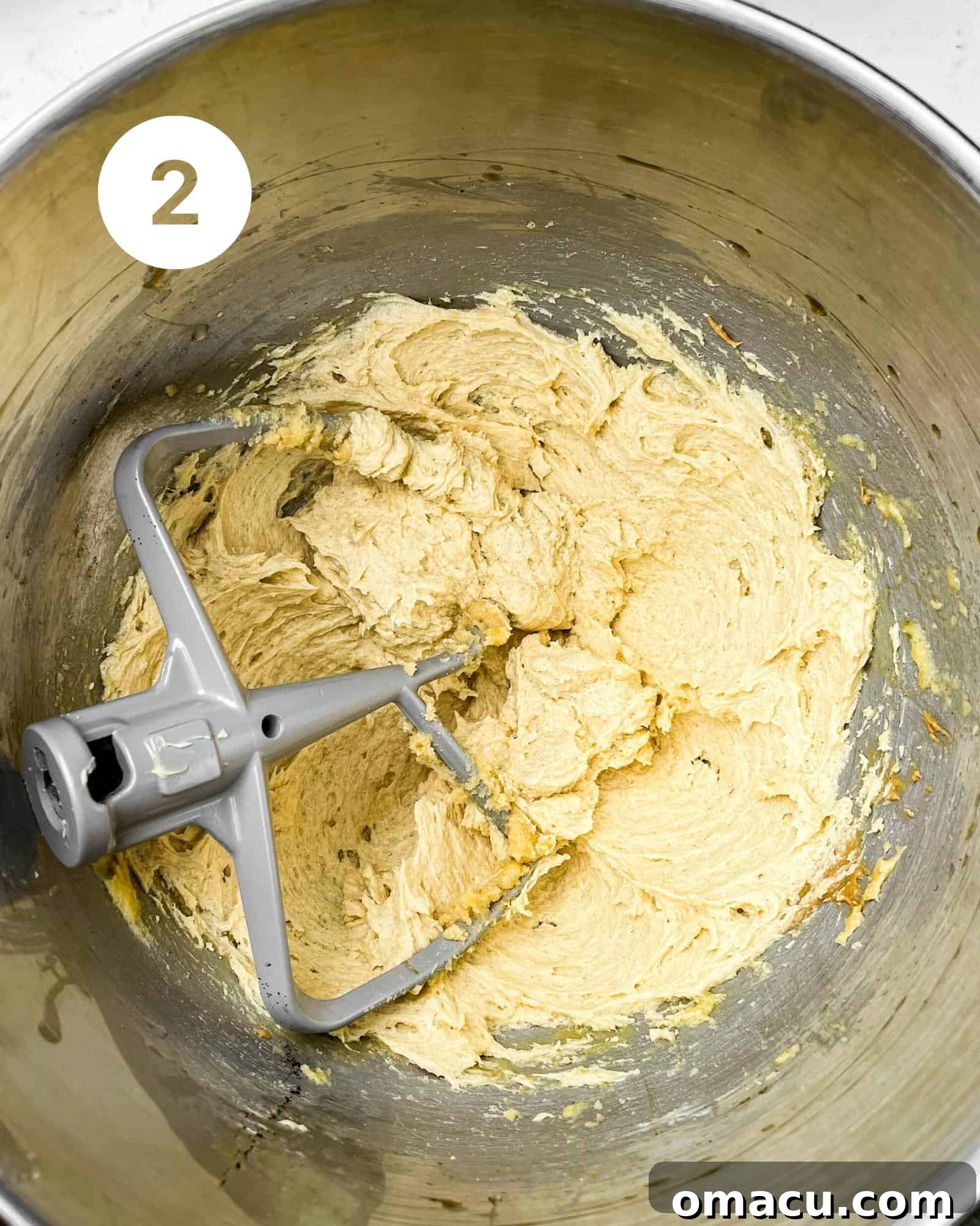 The wet ingredients, including softened butter, brown sugar, granulated sugar, creamy peanut butter, eggs, and vanilla extract, are being mixed to a light and fluffy consistency in a silver stand mixer bowl.