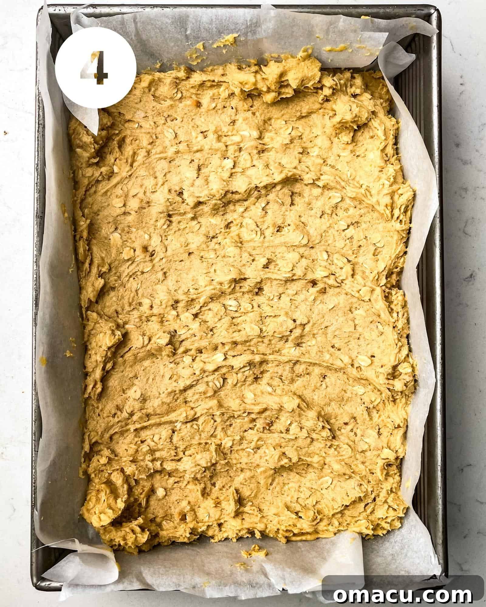 The peanut butter oatmeal cookie dough is evenly pressed into a 9x13 inch baking pan lined with parchment paper, forming the base for the bars.