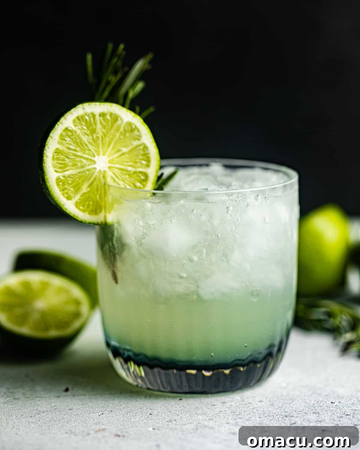 A perfectly crafted vodka gimlet cocktail on a grey surface, garnished with a vibrant lime wheel and fresh rosemary sprig.