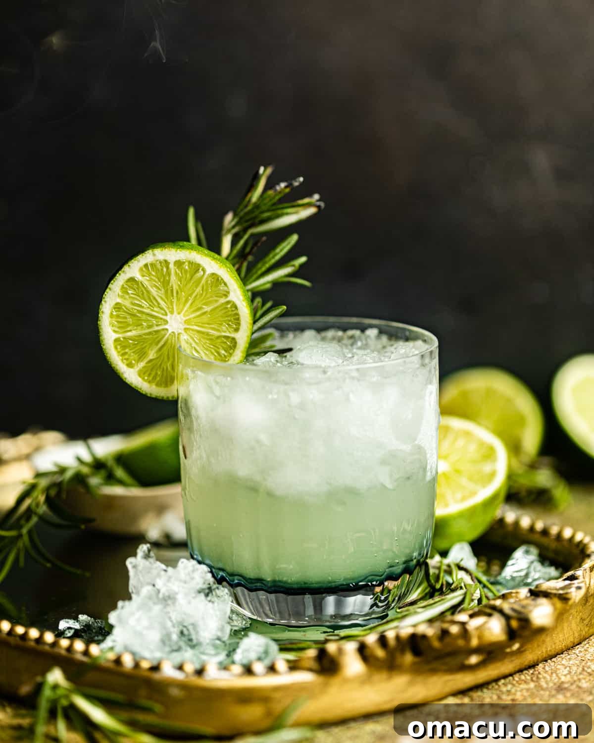 A vibrant vodka gimlet served in a coupe glass on a gleaming gold tray, surrounded by crushed ice for extra chill.