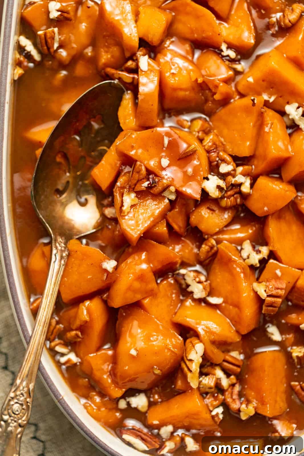 A glistening casserole dish filled with golden-brown candied sweet potatoes, ready to be served, with a spoon resting inside.