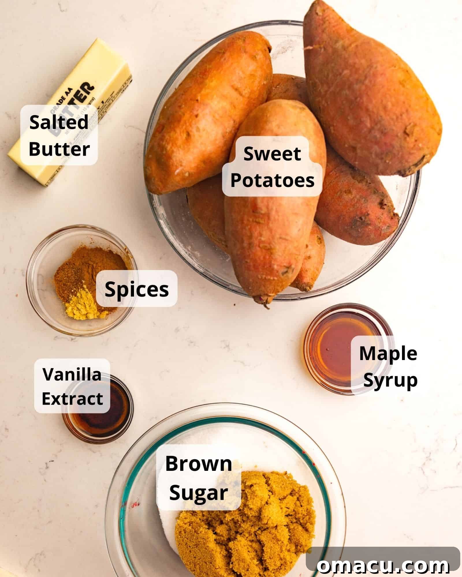 A flat lay photograph showcasing all the key ingredients needed to make candied sweet potatoes: fresh sweet potatoes, maple syrup, dark brown sugar, butter, ground cinnamon, nutmeg, ginger, and a bottle of vanilla extract.