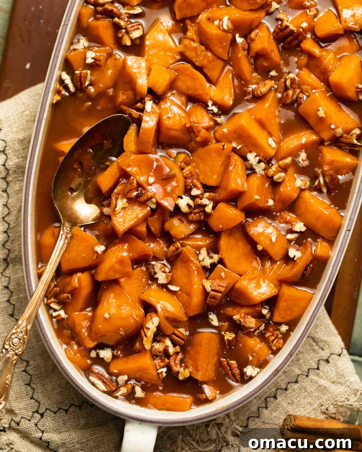 A serving dish filled with perfectly glazed candied sweet potatoes, adorned with a silver serving spoon, ready to be enjoyed.