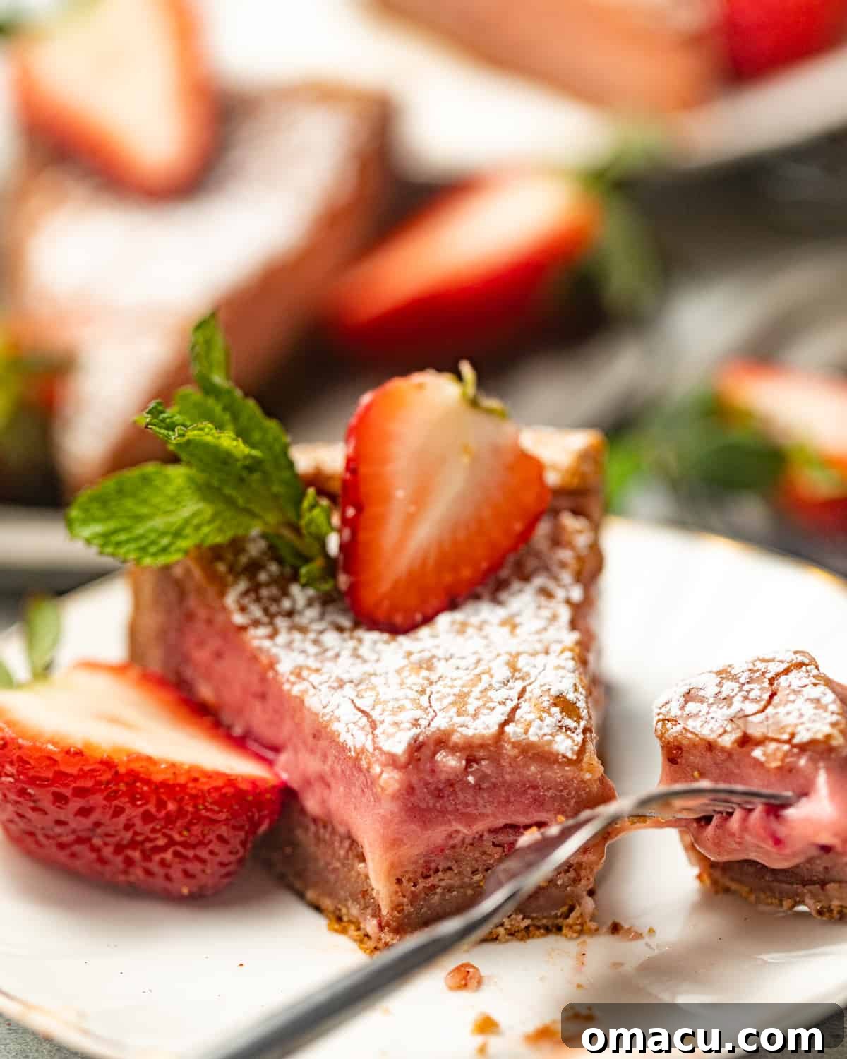 Sliced Strawberry Butter Cake on a white plate with a fork and a fresh strawberry on top, showcasing the gooey center.