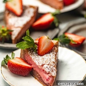A slice of strawberry butter cake on a white plate with a sliced strawberry on top, showcasing the dessert's deliciousness.