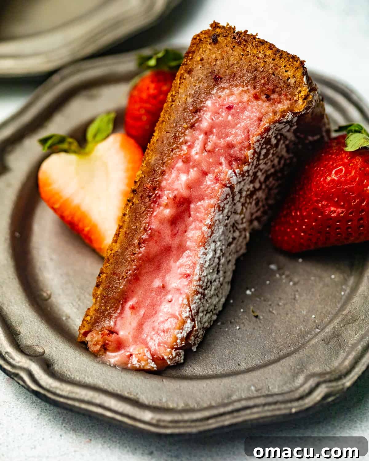 Close-up of a sliced strawberry ooey gooey cake on a silver plate, showing the distinct layers of cake and creamy filling.