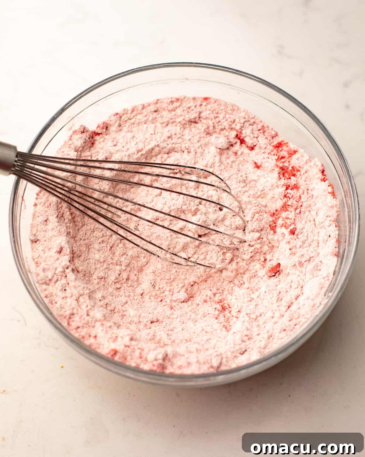 Flour, baking powder, salt, and strawberry powder whisked together in a bowl, creating a pinkish dry mix.