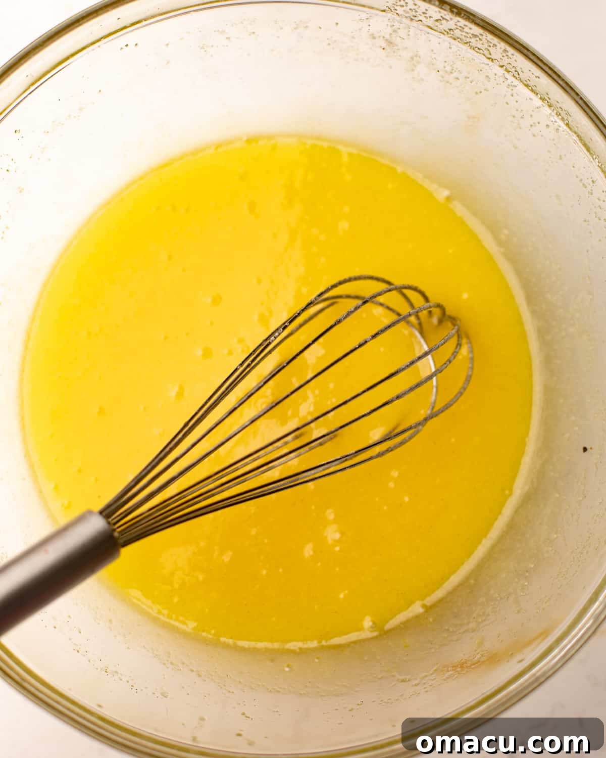 Melted butter and sugar whisked together in a bowl, a crucial step for the cake base.