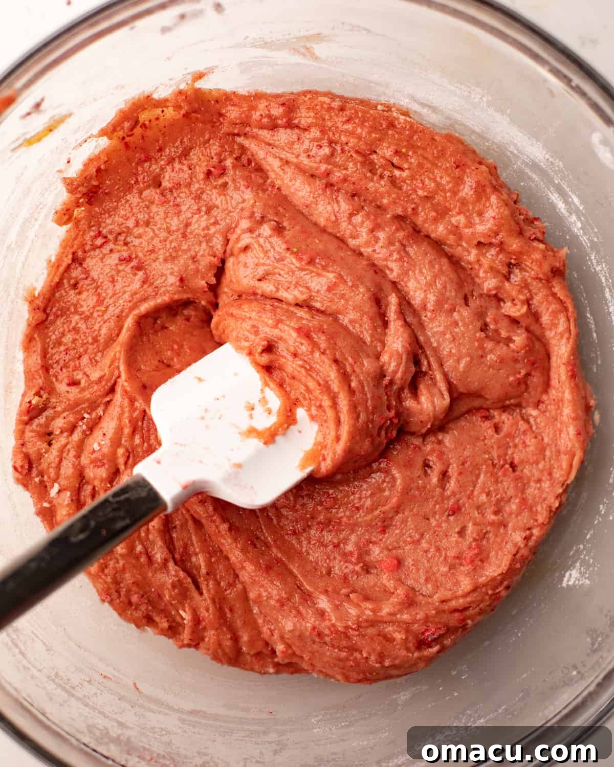 Strawberry cake batter mixed together in a bowl with a flat spatula, ready to be spread into the pan.