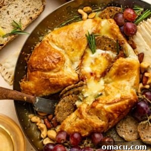 baked brie in puff pastry on a gold plate with grapes and crackers.